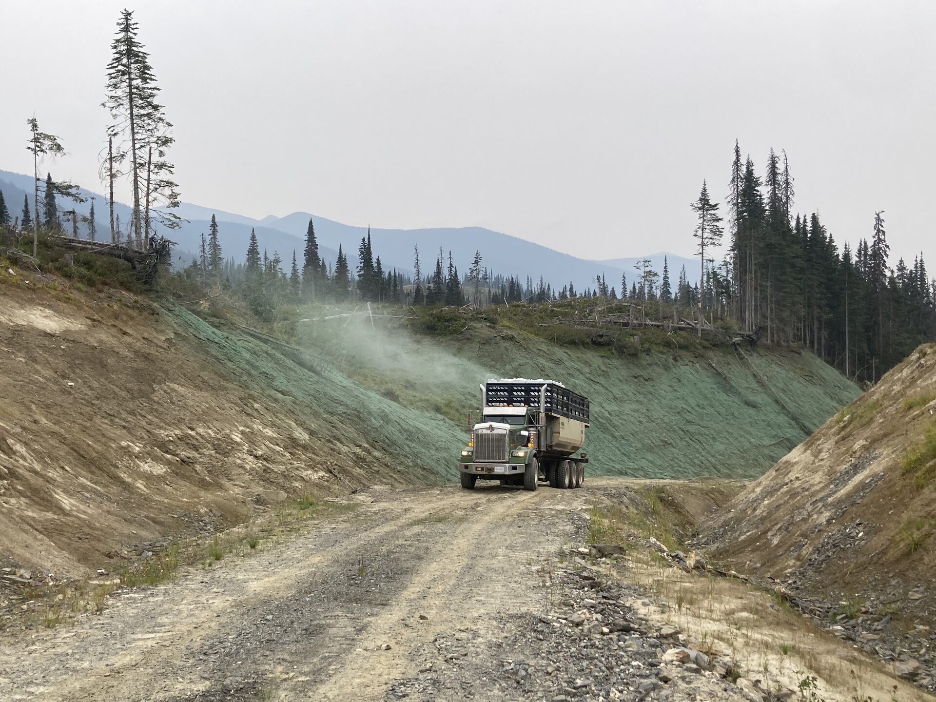 Hydroseeding truck working a gravel resource road between freshly seeded cut slopes, BC